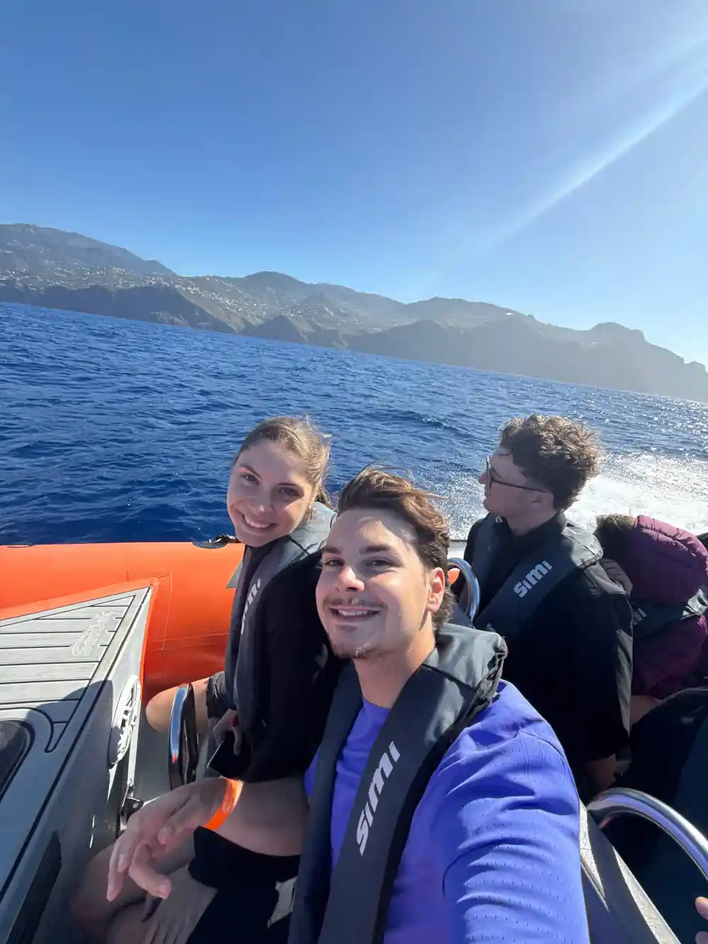 three guests in life jackets grinning from the rib with mountains behind
